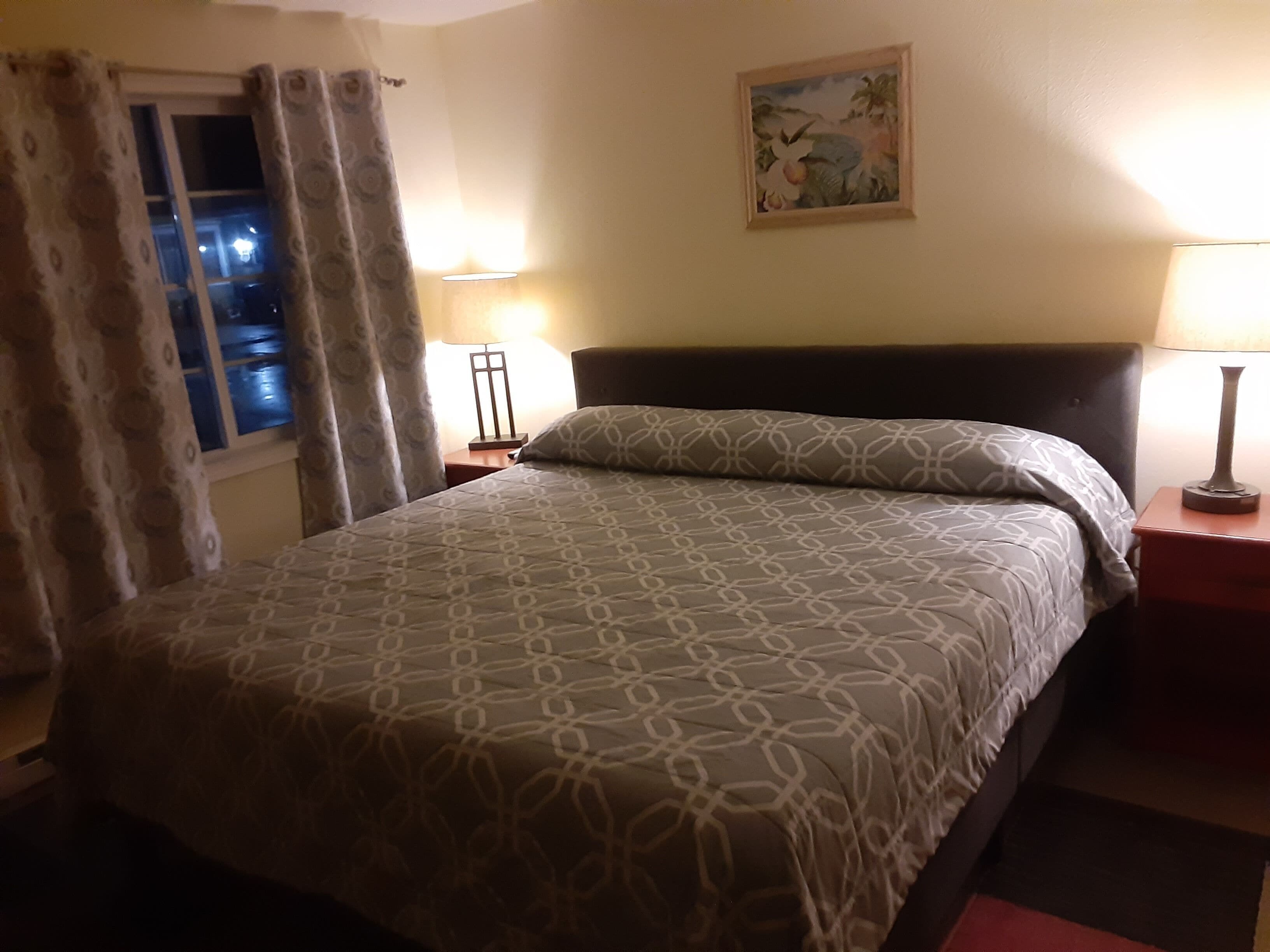 Una habitación de hotel con cama, dos lámparas de noche, una ventana con cortinas y un cuadro en la pared.