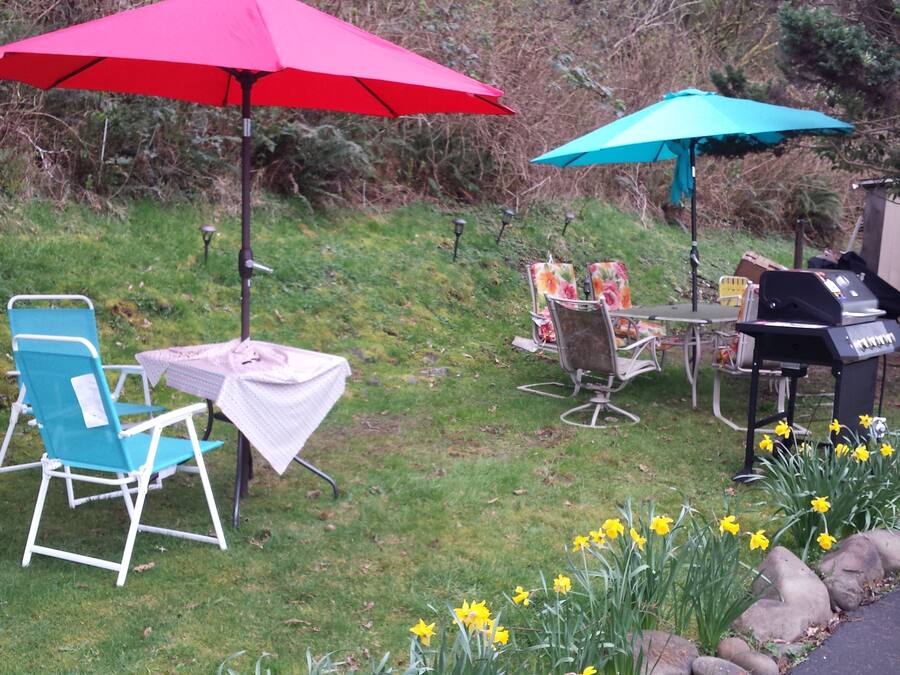 Eine Terrasse im Freien mit einem blauen Stuhl, einem Tisch mit weißer Tischdecke, einem roten Sonnenschirm, einem blauen Sonnenschirm und einem Grill.