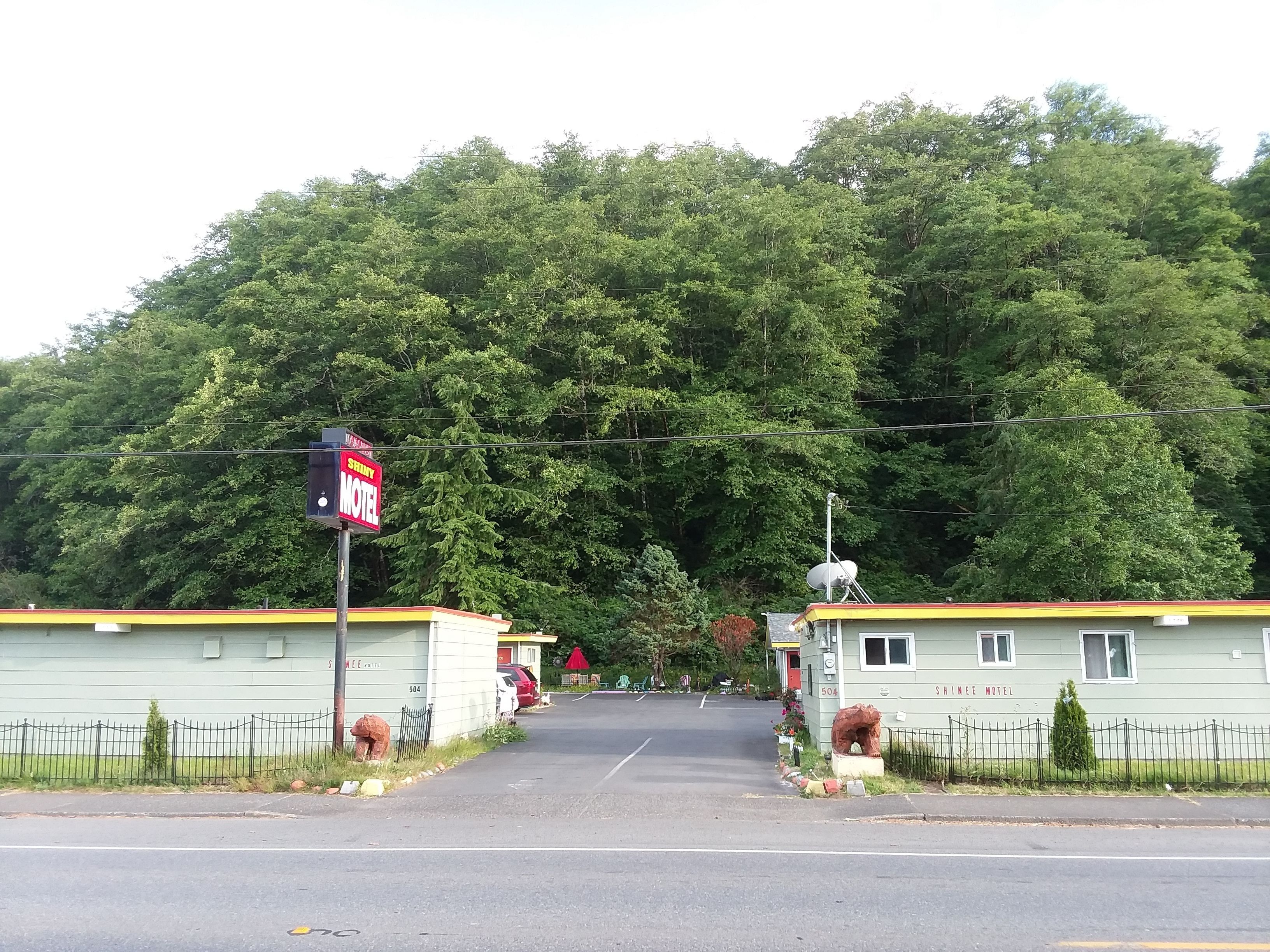 A motel with a signboard, a road leading to it, and a forested hill in the background.