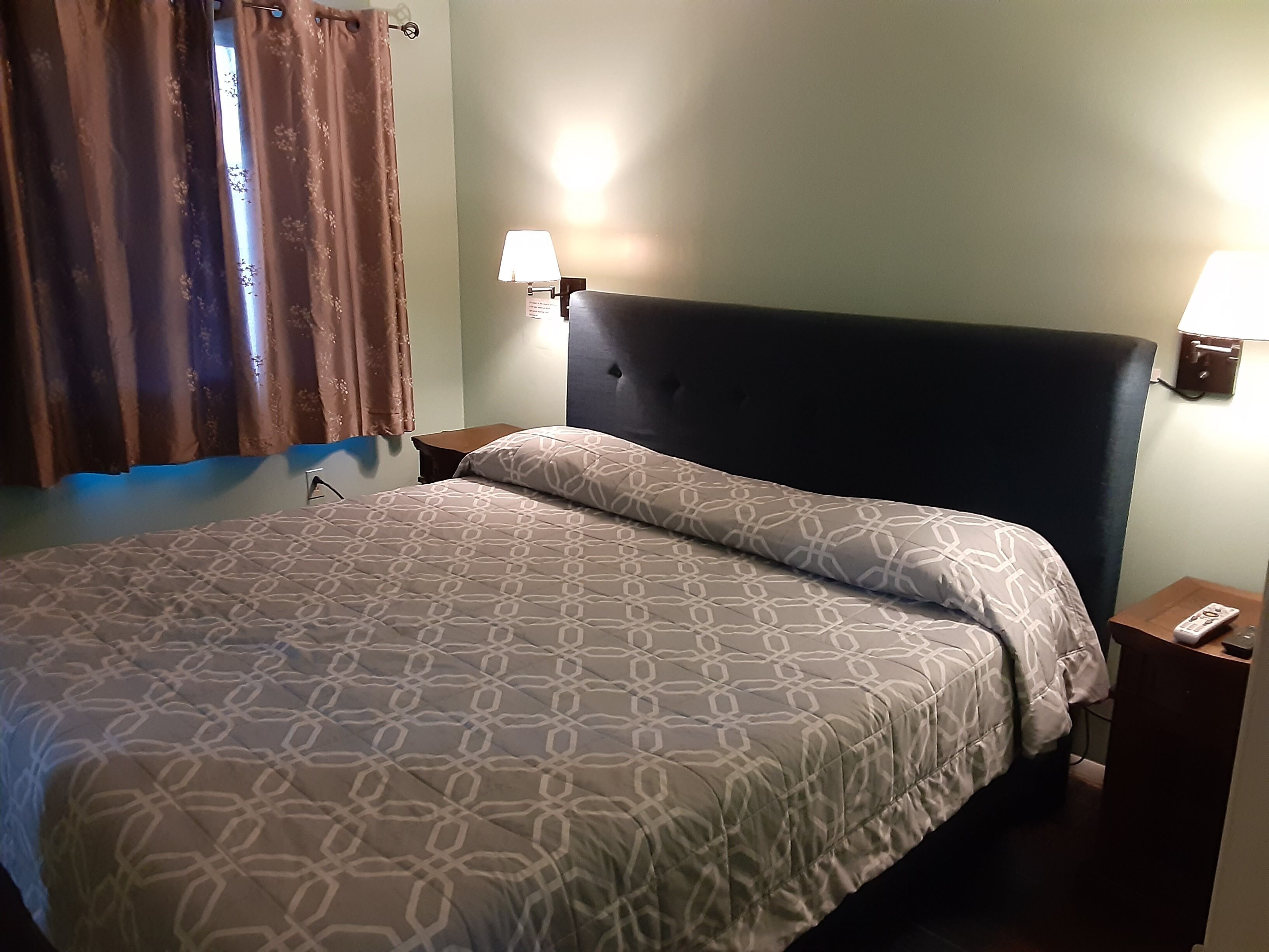 A hotel room with a large bed, two bedside lamps, a nightstand, and a window with curtains.