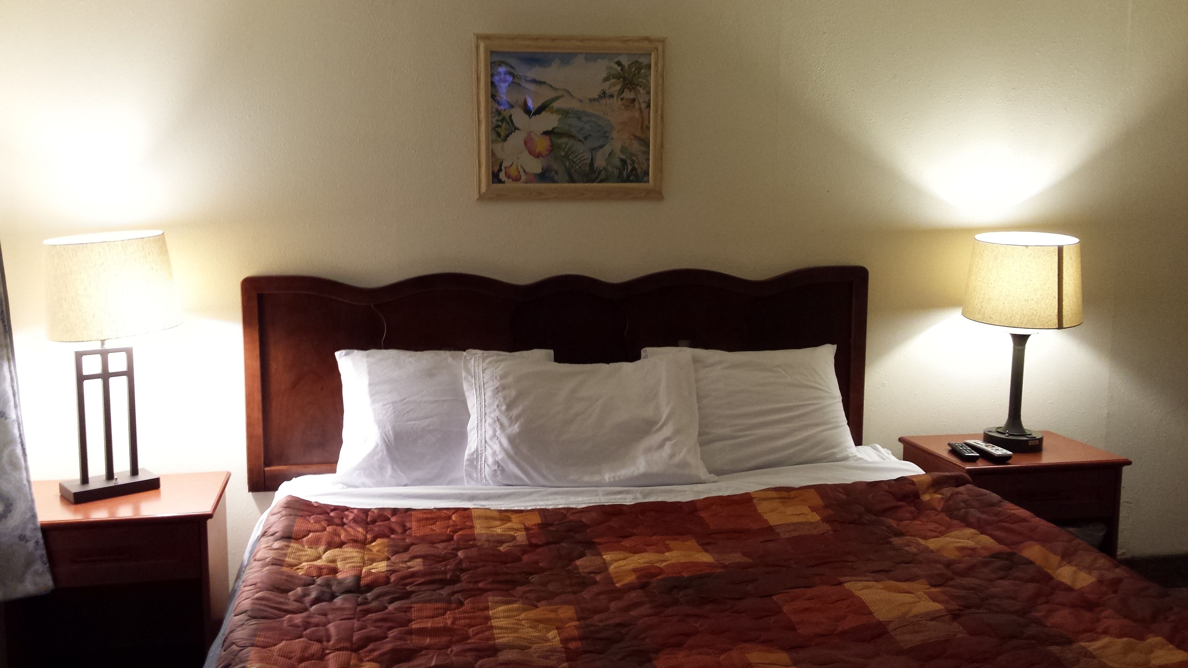 A hotel room with a bed, two bedside lamps, a nightstand, and a painting on the wall.