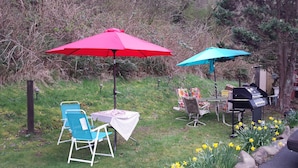 An outdoor patio with two umbrellas, a grill, and a table with chairs. - Shiny Motel (Hoquiam)
