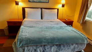A neatly made bed with a patterned duvet, two bedside tables with lamps, a painting of birds on the wall, and a window with curtains. - Shiny Motel (Hoquiam)