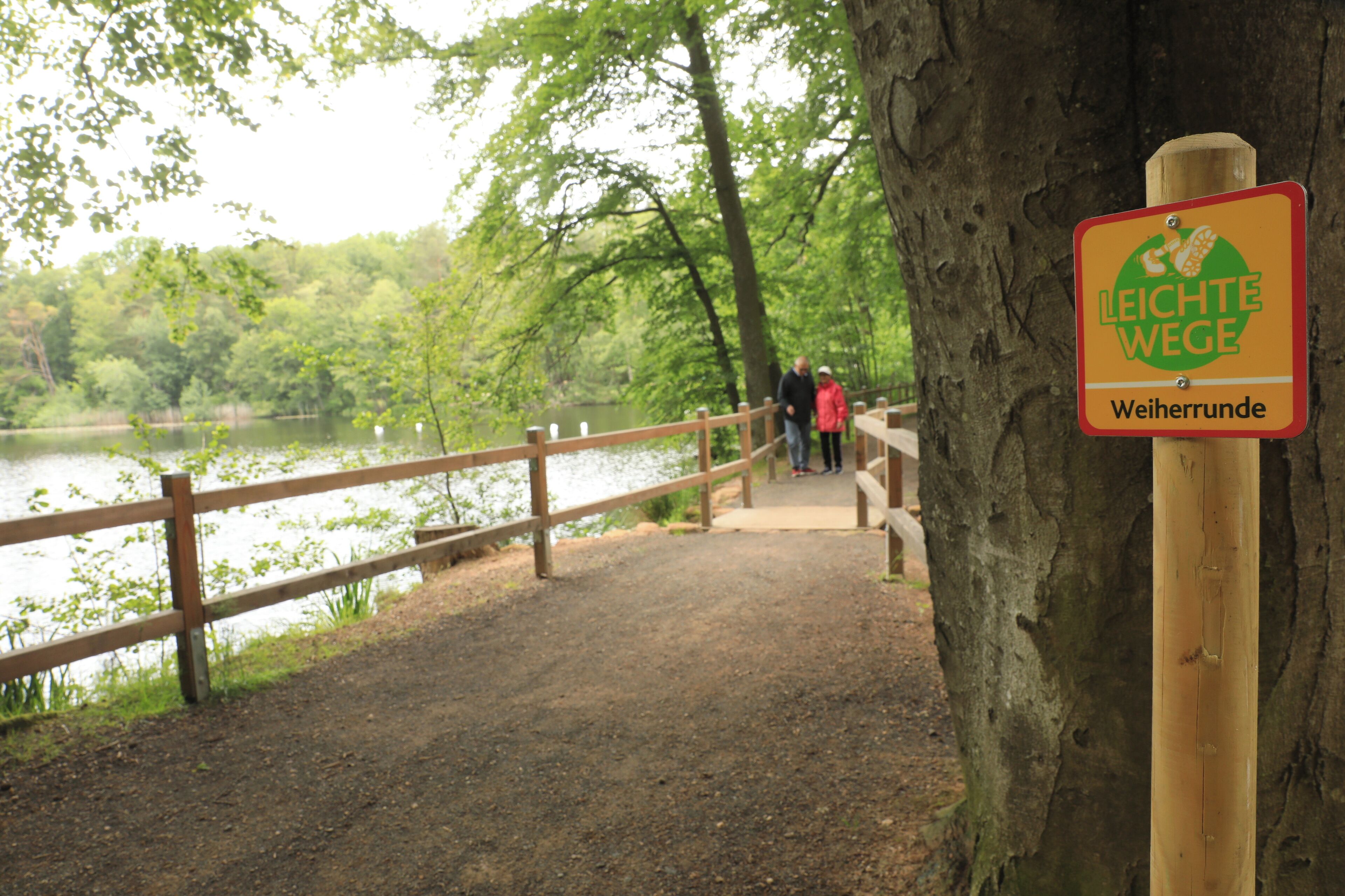 Un puente de madera sobre un lago, con un cartel que dice 'Leichte Wege Weiherrunde'.
