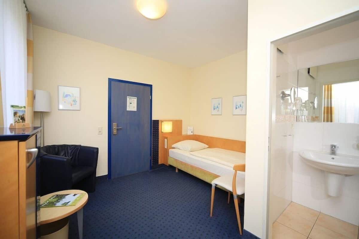 Ein Hotelzimmer mit einem Bett, einem Schreibtisch, einem Sessel, einem kleinen Tisch, einem Waschbecken und einer Tür.
