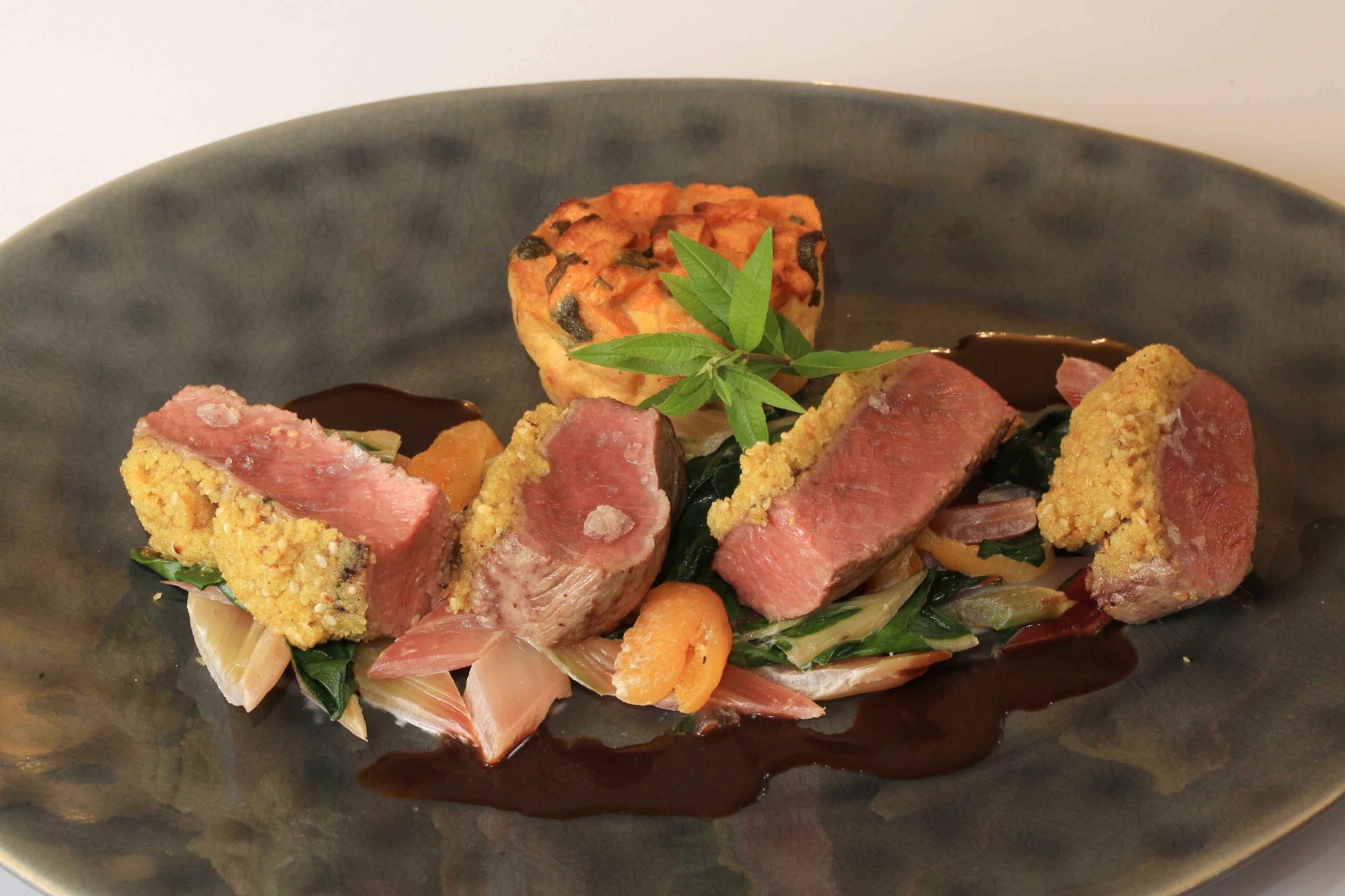 A dish with meat, vegetables, and a small green garnish on a plate.