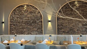 Un restaurant dont le décor est agrémenté d’un mur en pierre, de sièges confortables et de tables soigneusement dressées.