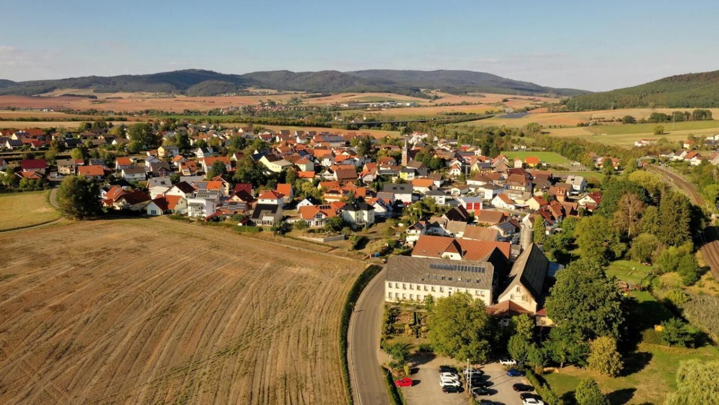 Eine Vogelperspektive einer kleinen Stadt mit einer Mischung aus Wohn- und Geschäftsgebäuden, umgeben von Feldern und Hügeln.