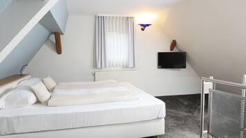 A bedroom with a bed, a window with curtains, a wall-mounted TV, and a radiator.