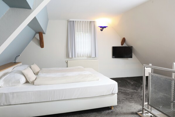 A bedroom with a bed, a window with curtains, a wall-mounted TV, and a radiator. - Landidyll Hotel Klostermühle (Muenchweiler an der Alsenz)