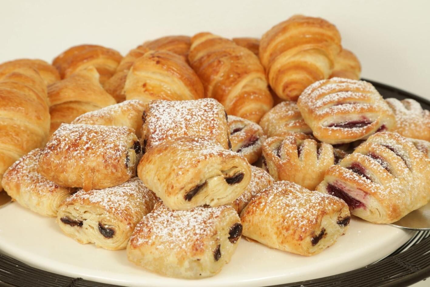A plate of pastries, including croissants and filled pastries dusted with powdered sugar.