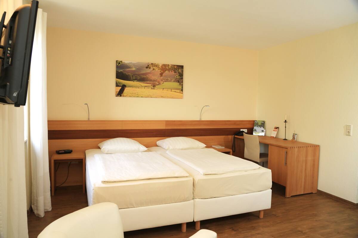 Ein Hotelzimmer mit Doppelbett, Schreibtisch, Stuhl, Nachttisch und einem Bild an der Wand.