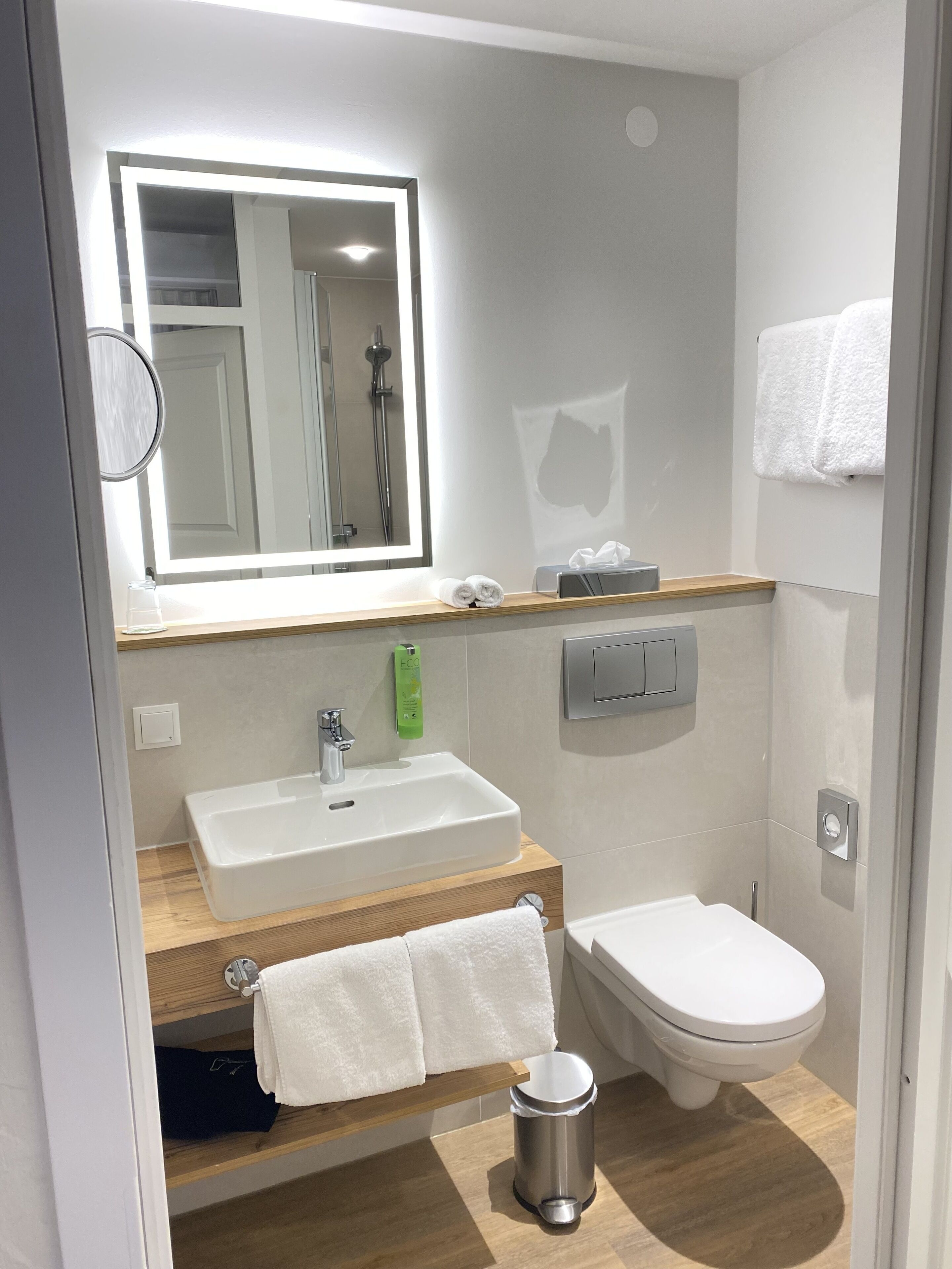 Un baño moderno con lavamanos, espejo, inodoro y un cubo de basura.