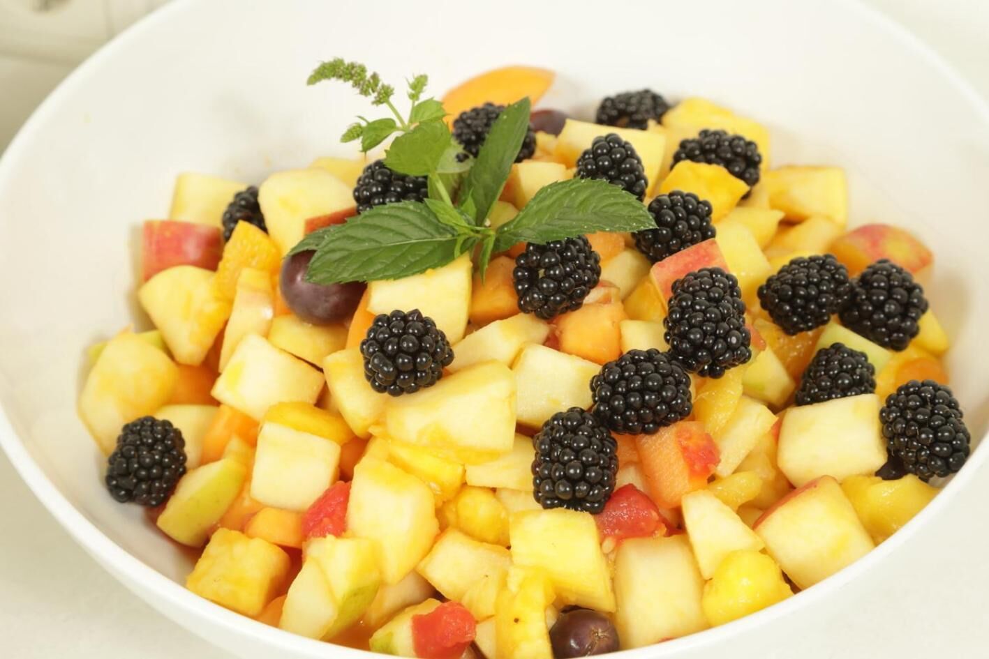 A bowl of fruit salad with blackberries and mint leaves.