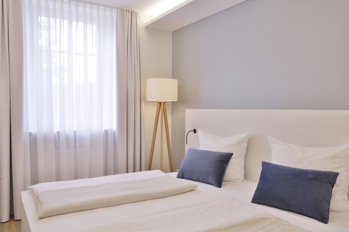 Ein Hotelzimmer mit einem großen Bett, einer Nachttischlampe und durchsichtigen Vorhängen.