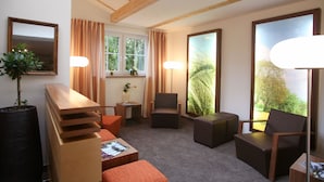 Une pièce moderne avec un plafond en bois, de grandes fenêtres et un coin salon comprenant une table et des chaises.