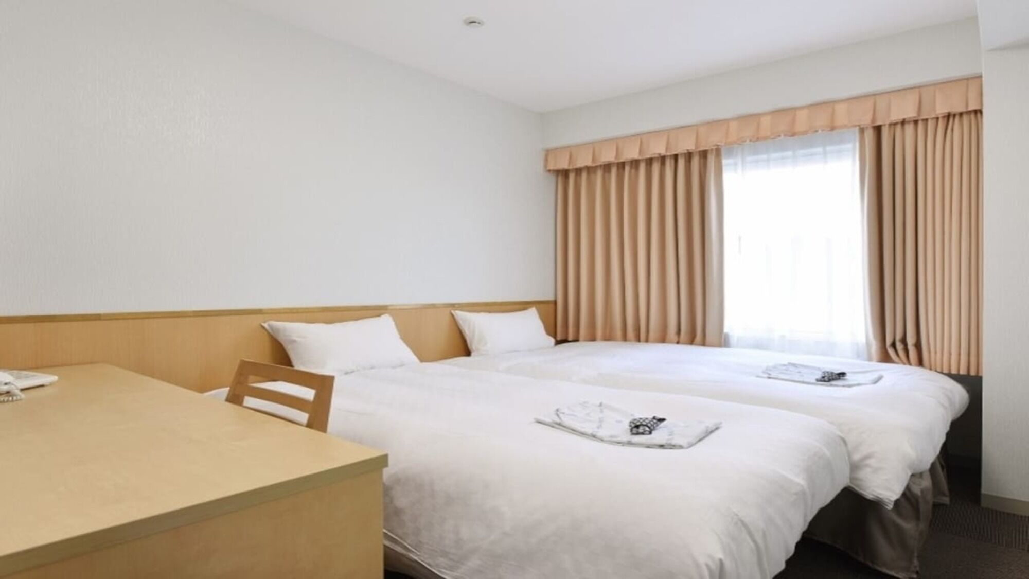 A hotel room with two beds, a wooden desk, and a window with curtains.