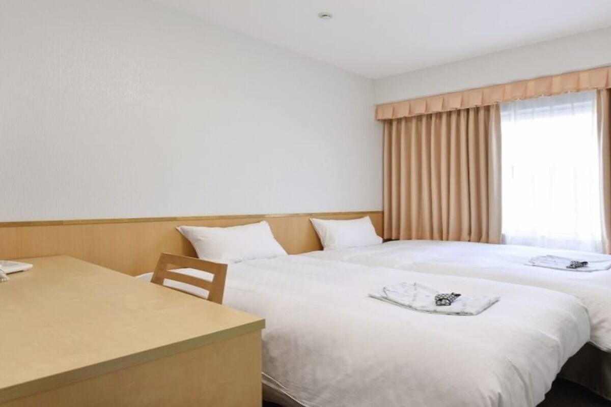 A hotel room with two beds, a wooden desk, and a window with curtains.
