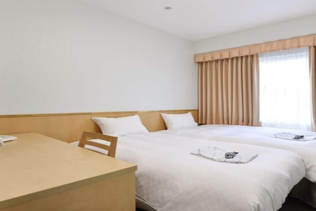 Una habitación de hotel con dos camas, un escritorio de madera y un ventanal con cortinas.