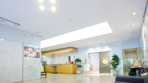 Un moderno vestíbulo de hotel con una recepción, un área de descanso y un amplio ventanal que permite la entrada de luz natural.