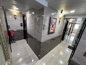 A modern hotel lobby with marble walls, a framed picture, and a fire extinguisher. - Victoria Inn (Kowloon)