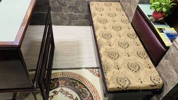A hotel room with a bed, a small table with a plant, and a tiled floor with a decorative border.