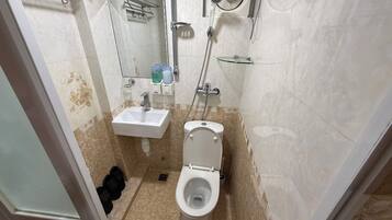 Et badeværelse med toilet, vask, bruser og et spejl.