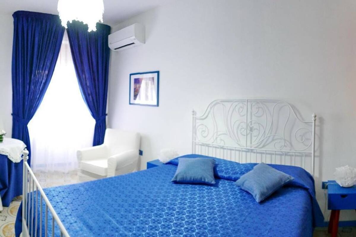 A bedroom with a white metal bed frame, blue bedding, a white chair, and a picture on the wall.