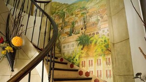 A staircase with a mural of a town on the wall. - Hotel Restaurant Le Bellevue (Bormes-Les-Mimosas)