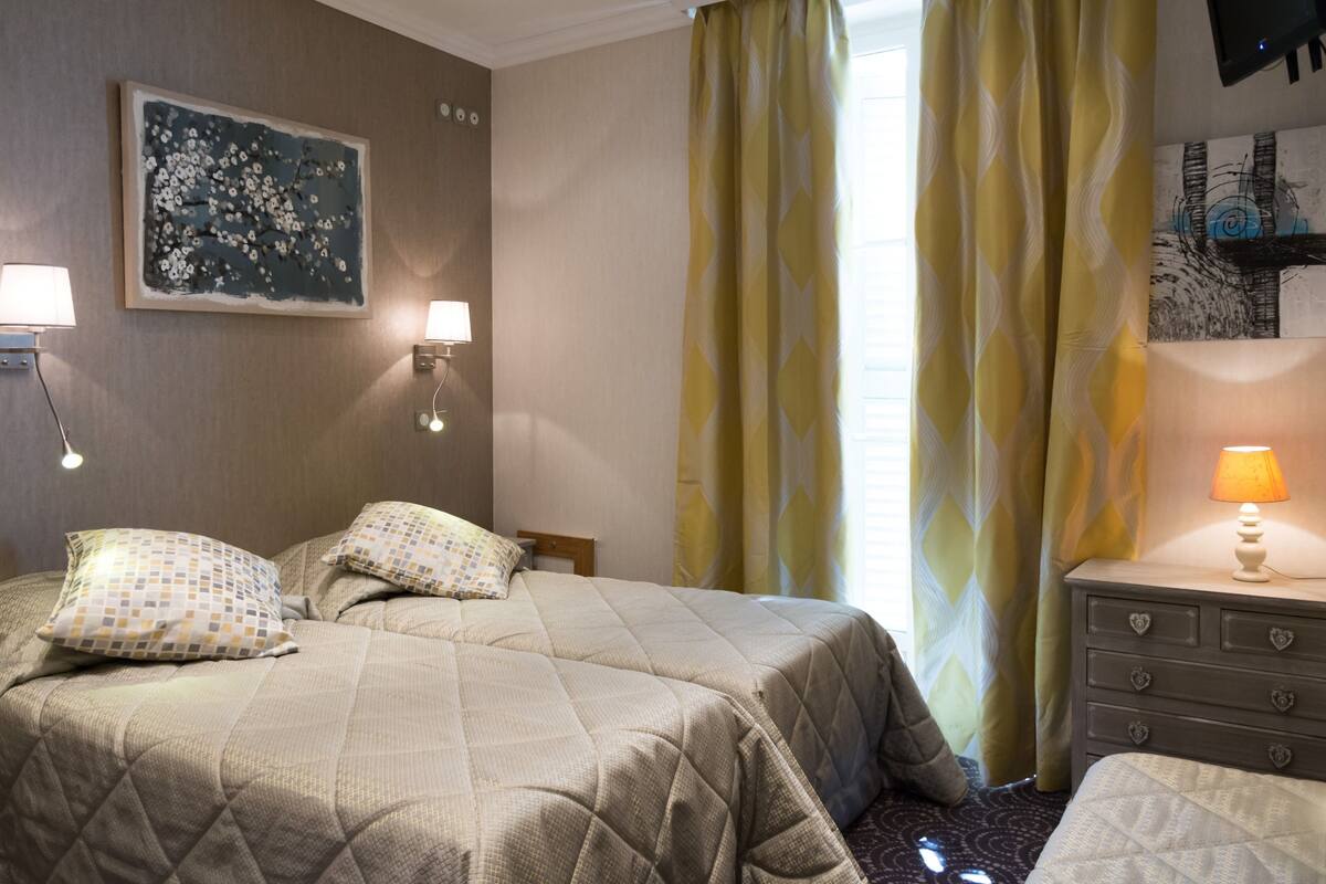 Una habitación de hotel con cama, tocador, lámpara, un cuadro y cortinas.