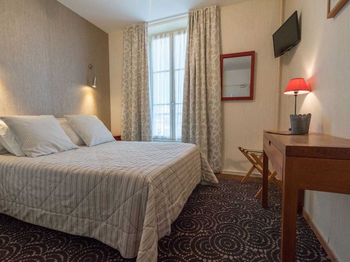 A hotel room with a bed, a desk, a TV, and a window with curtains.