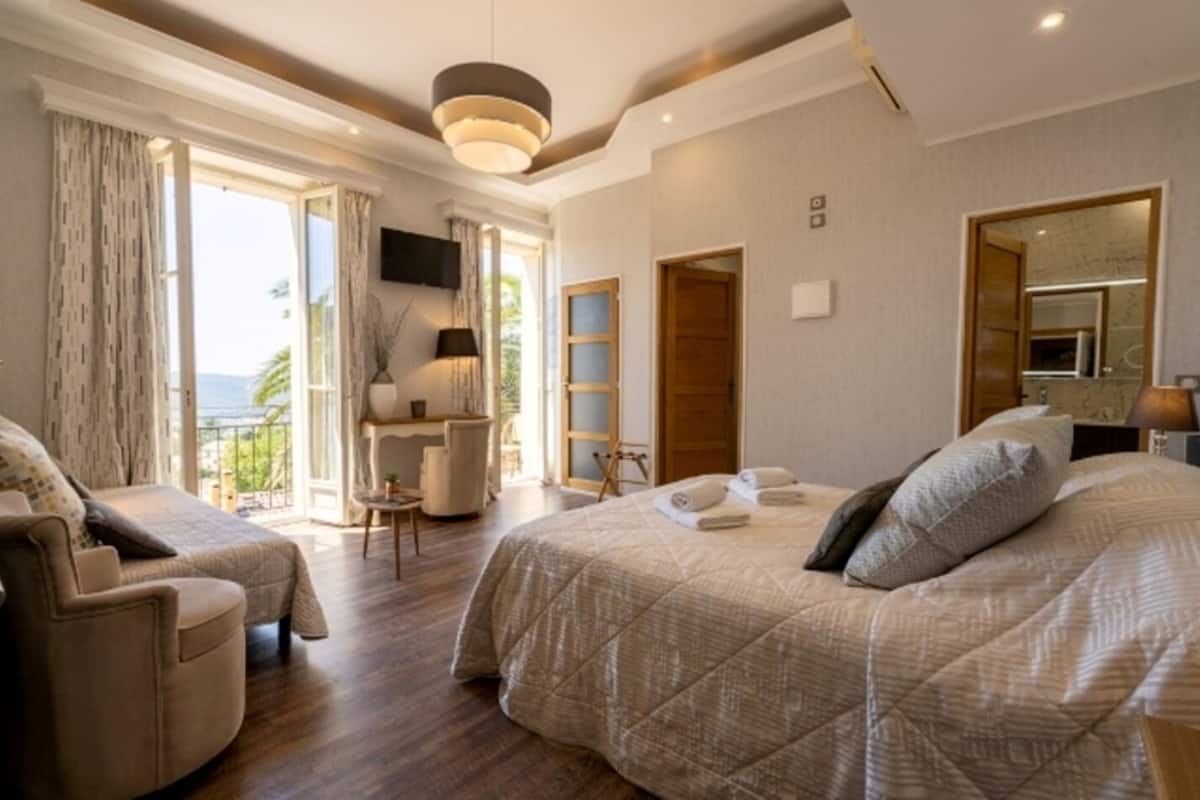 Habitación de hotel con una cama grande, un área de descanso con una silla, un escritorio y un balcón con vistas.