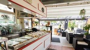 A café with a glass display case filled with pastries, a counter with a menu, and outdoor seating with wicker furniture. - Hotel Restaurant Le Bellevue (Bormes-Les-Mimosas)