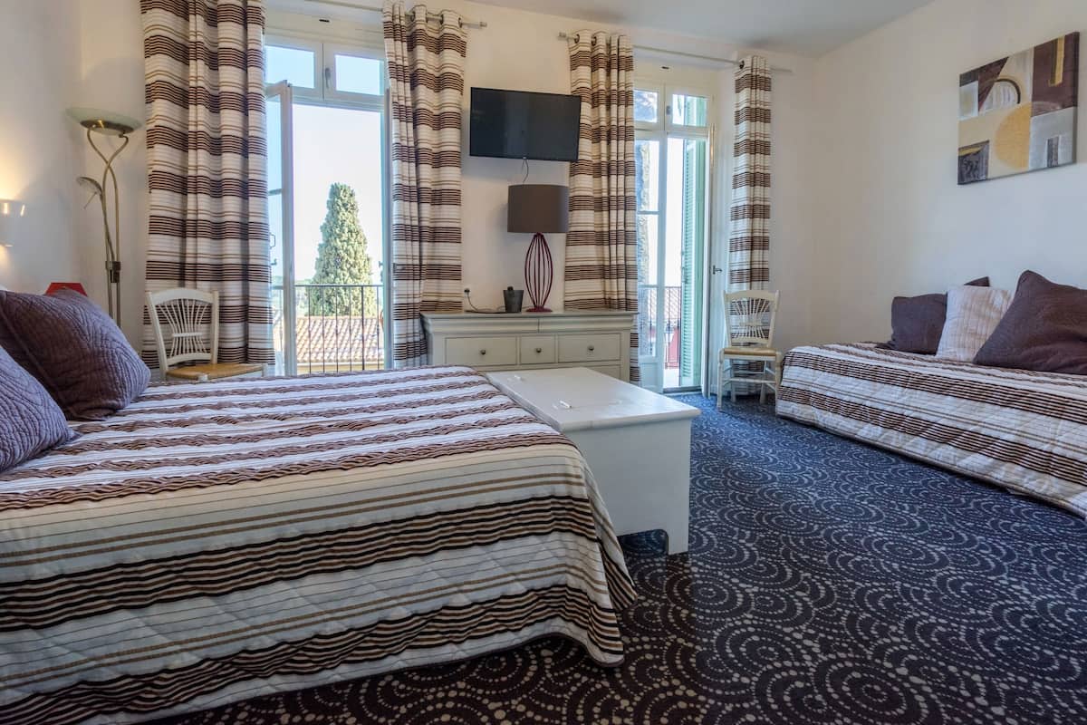 Habitación de hotel con dos camas, un escritorio, una silla, un televisor y un balcón con vistas.