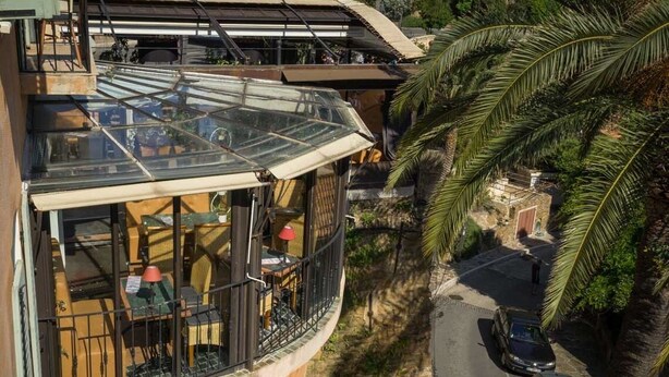 A glass-enclosed balcony with outdoor seating, surrounded by lush greenery. - Hotel Restaurant Le Bellevue (Bormes-Les-Mimosas)