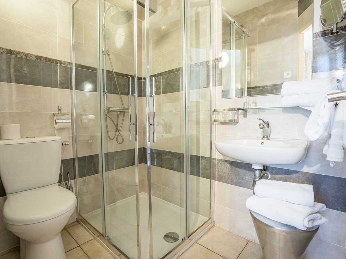 Un baño moderno con ducha de vidrio, inodoro y lavamanos con espejo.