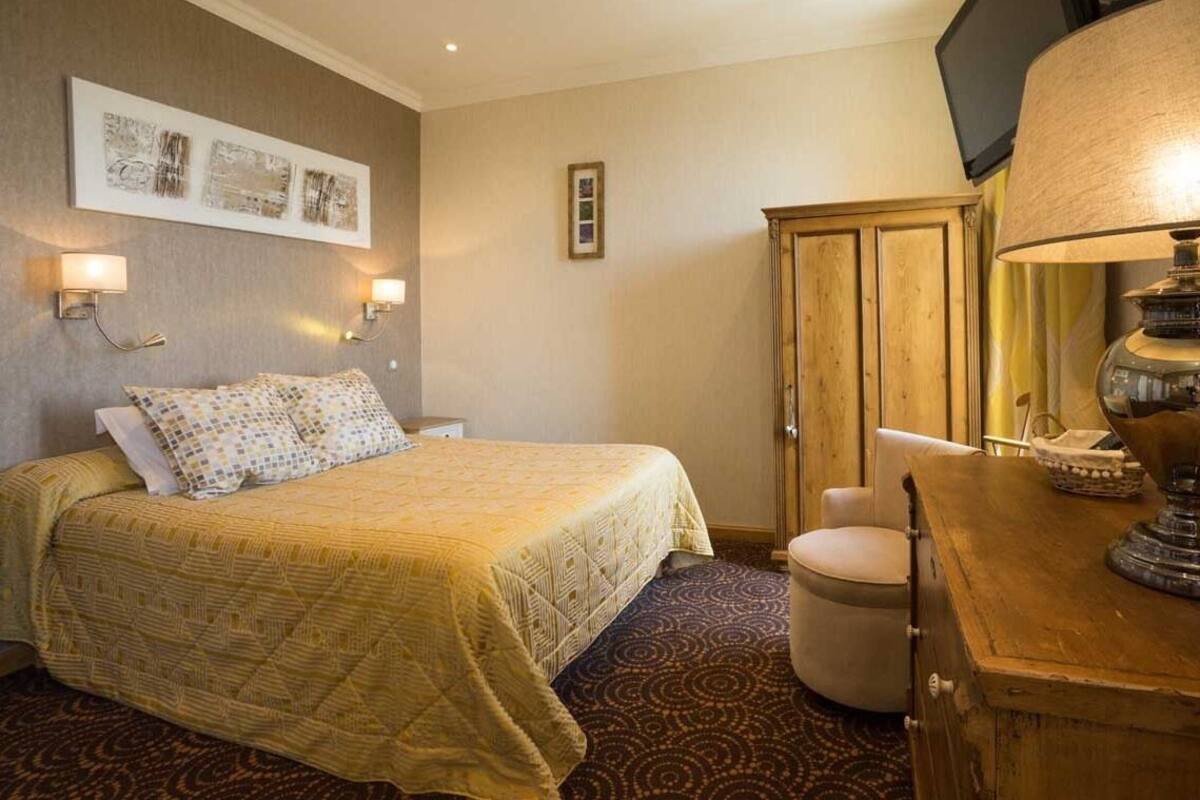 Habitación de hotel con cama, armario de madera, escritorio con lámpara e iluminación en la pared.