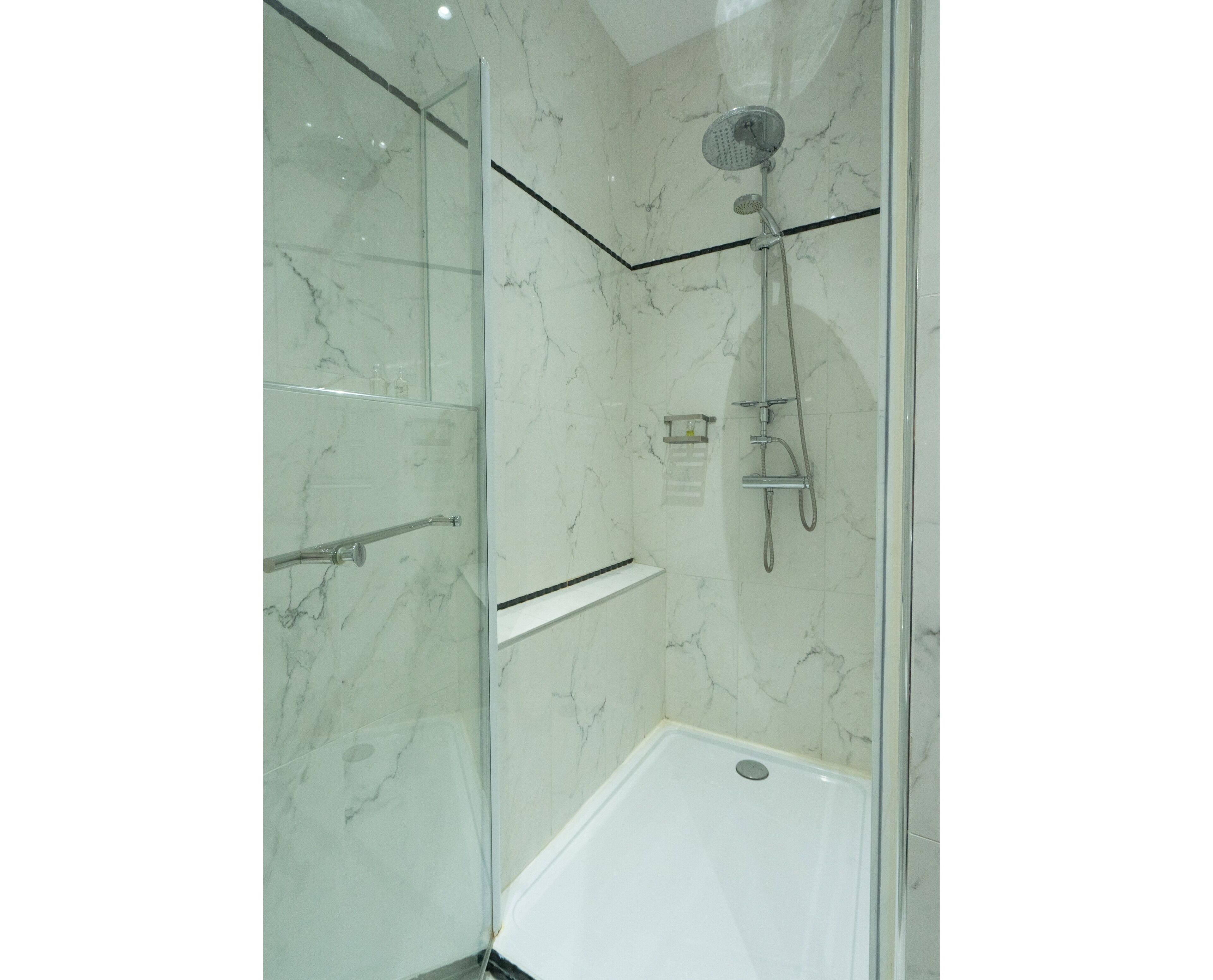 A glass-enclosed shower with a handheld showerhead and a wall-mounted faucet.