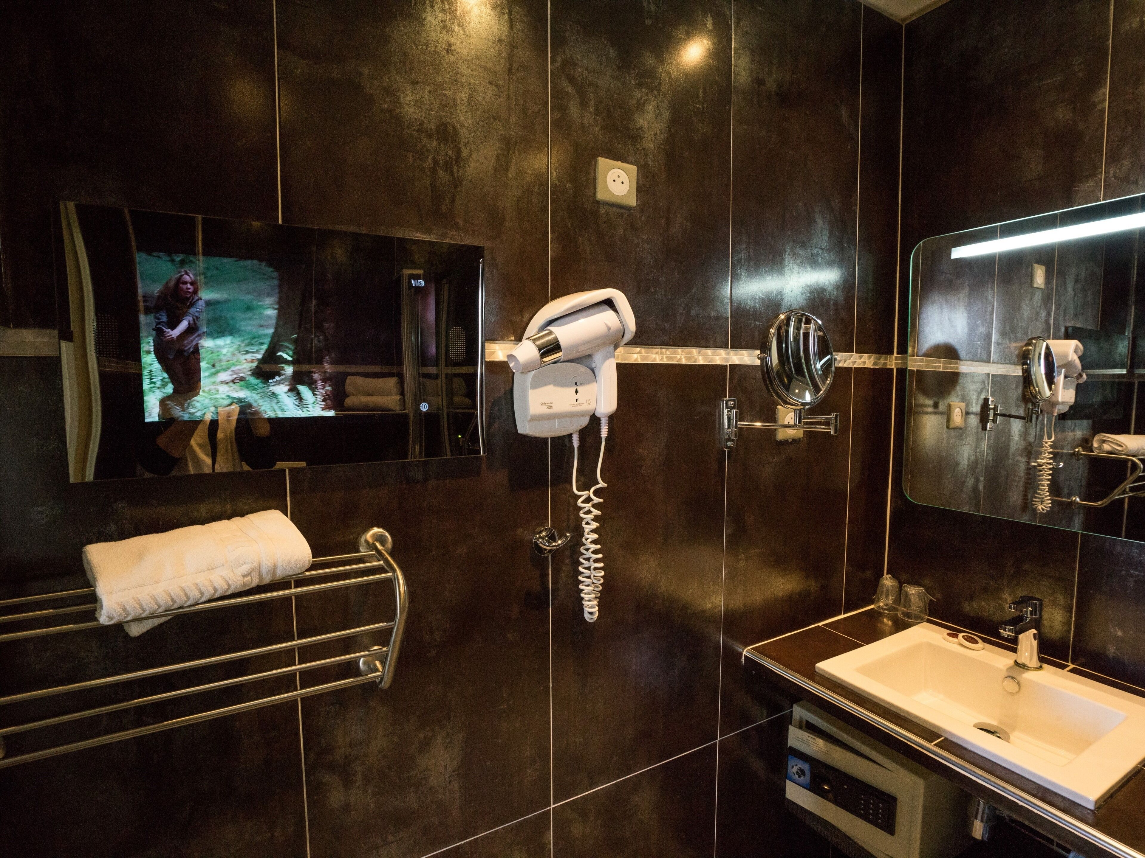 A modern bathroom with a large mirror, a hairdryer, a towel rack, and a sink.