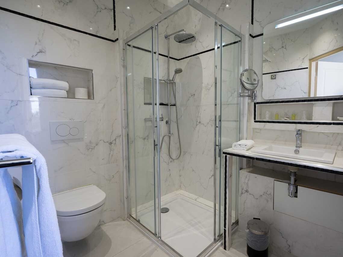 Et stilfuldt badeværelse med bruseniche i glas, toilet, vask med spejl og marmorvægge.