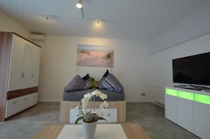 A modern living room with a sofa, a flat-screen TV, a decorative orchid vase, and a painting of a beach scene. - Apartment Leverkusen City  (Leverkusen)