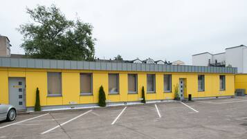 A yellow building with a grey roof, a parking lot, and a tree in the background.