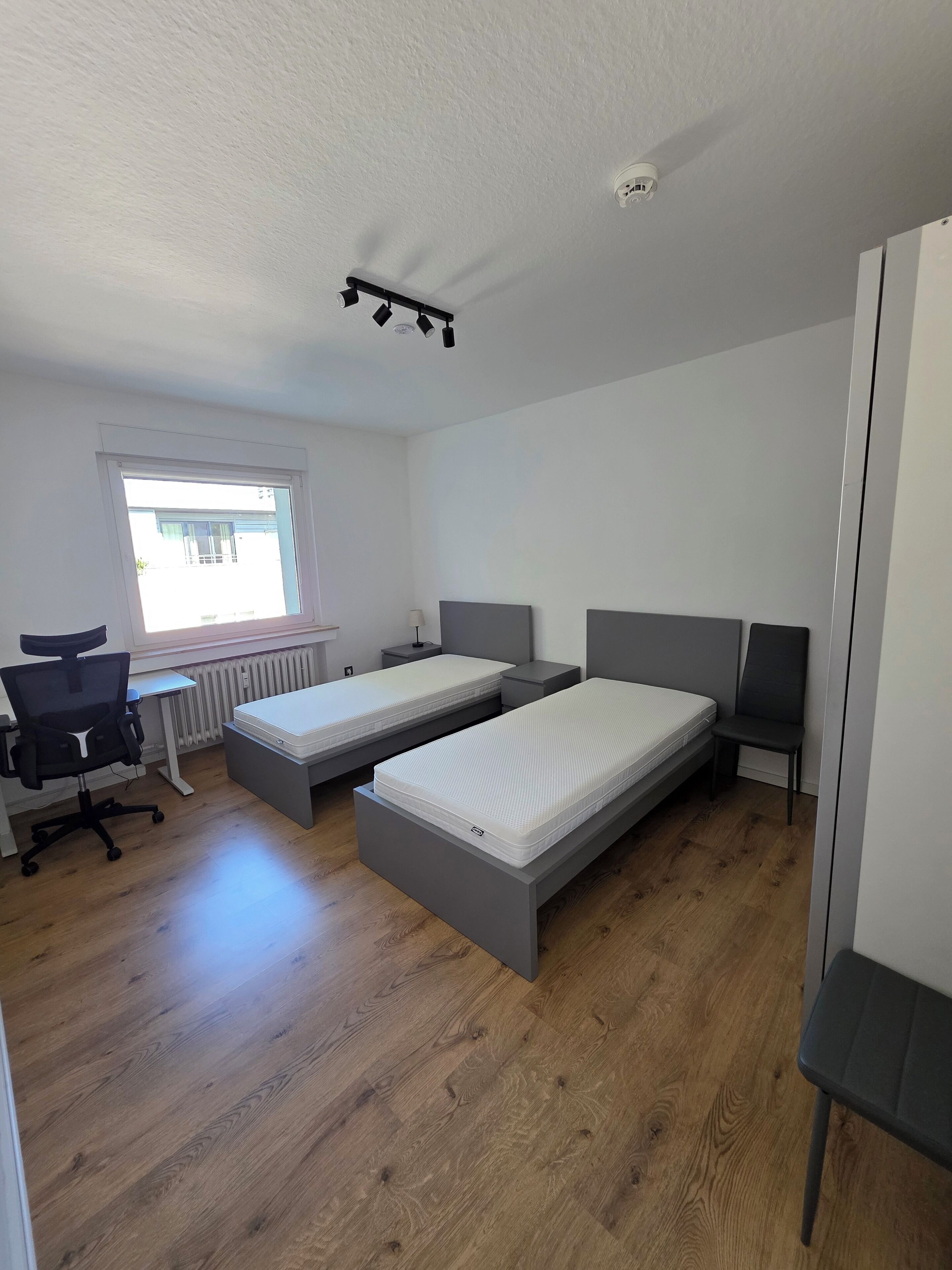 Ein modernes, kompaktes Zimmer mit zwei Einzelbetten, einem Schreibtisch und einem Stuhl.