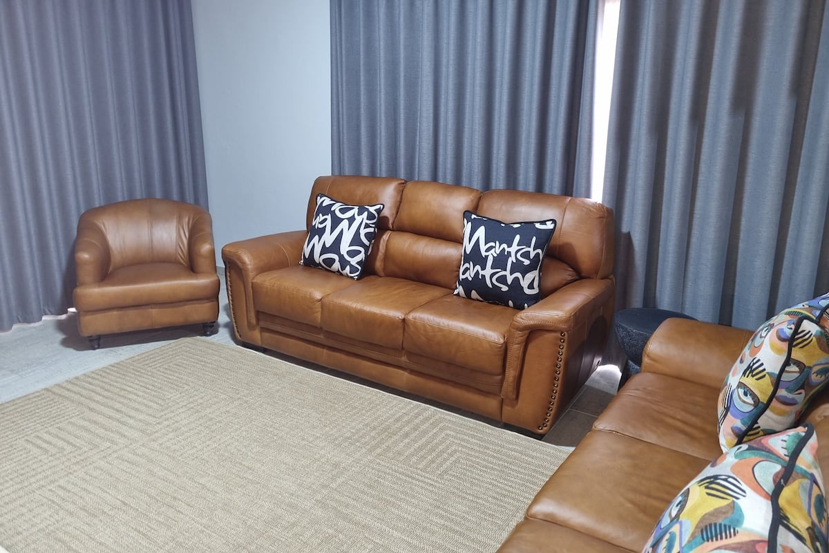 A living room with a brown leather sofa, two matching armchairs, and a patterned rug.