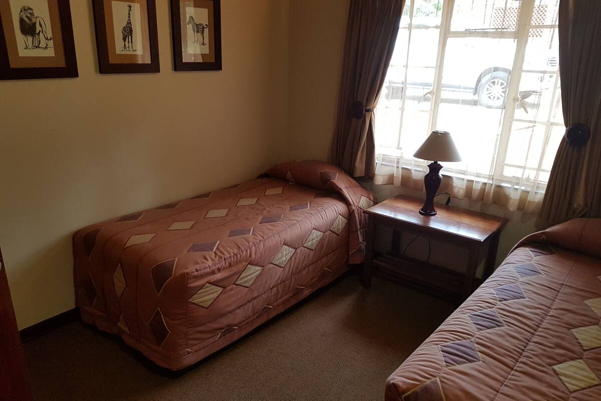 A room with two beds, a nightstand with a lamp, and framed animal pictures on the wall.