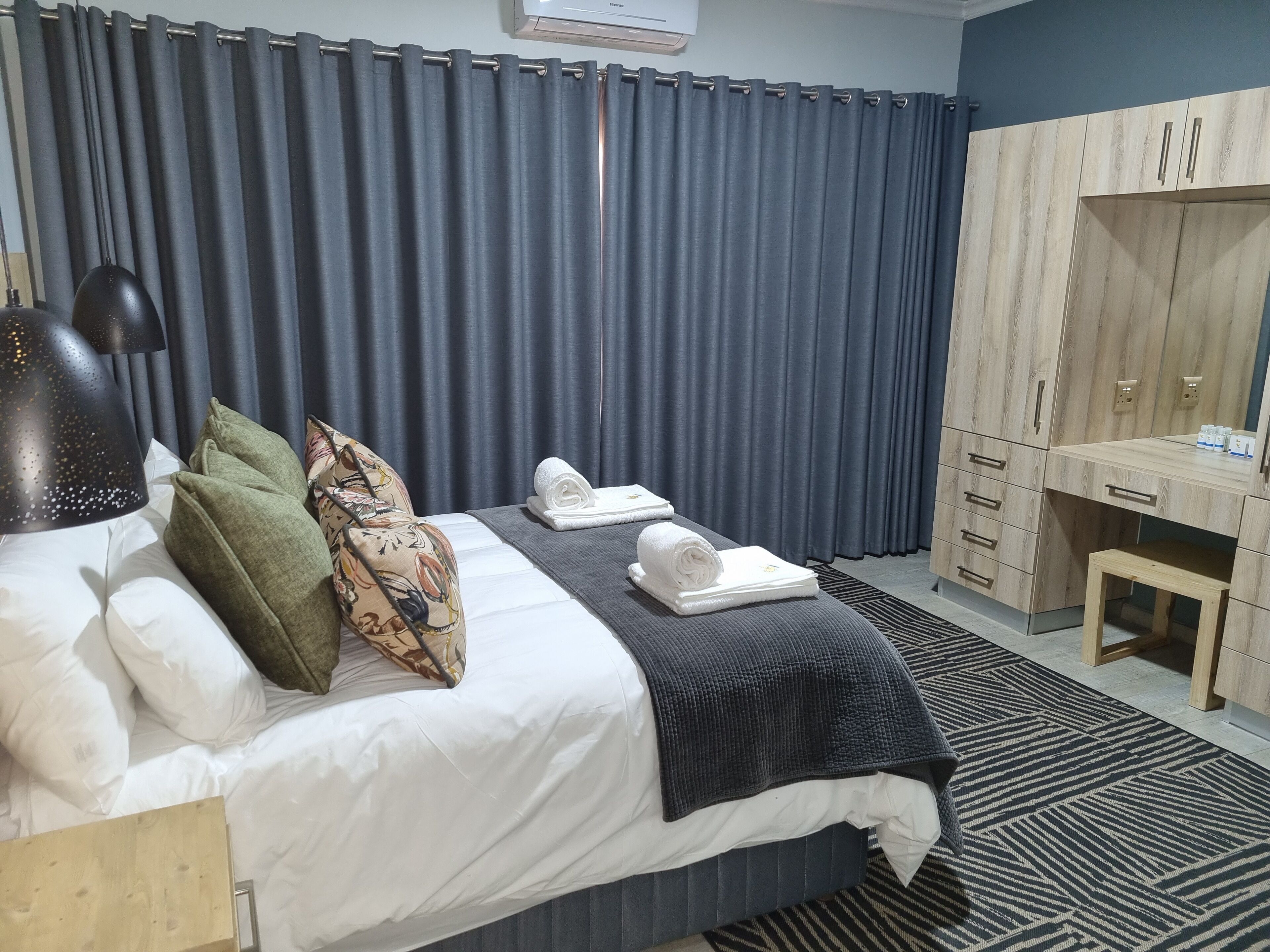 A hotel room with a bed, pillows, a desk, and a wardrobe.