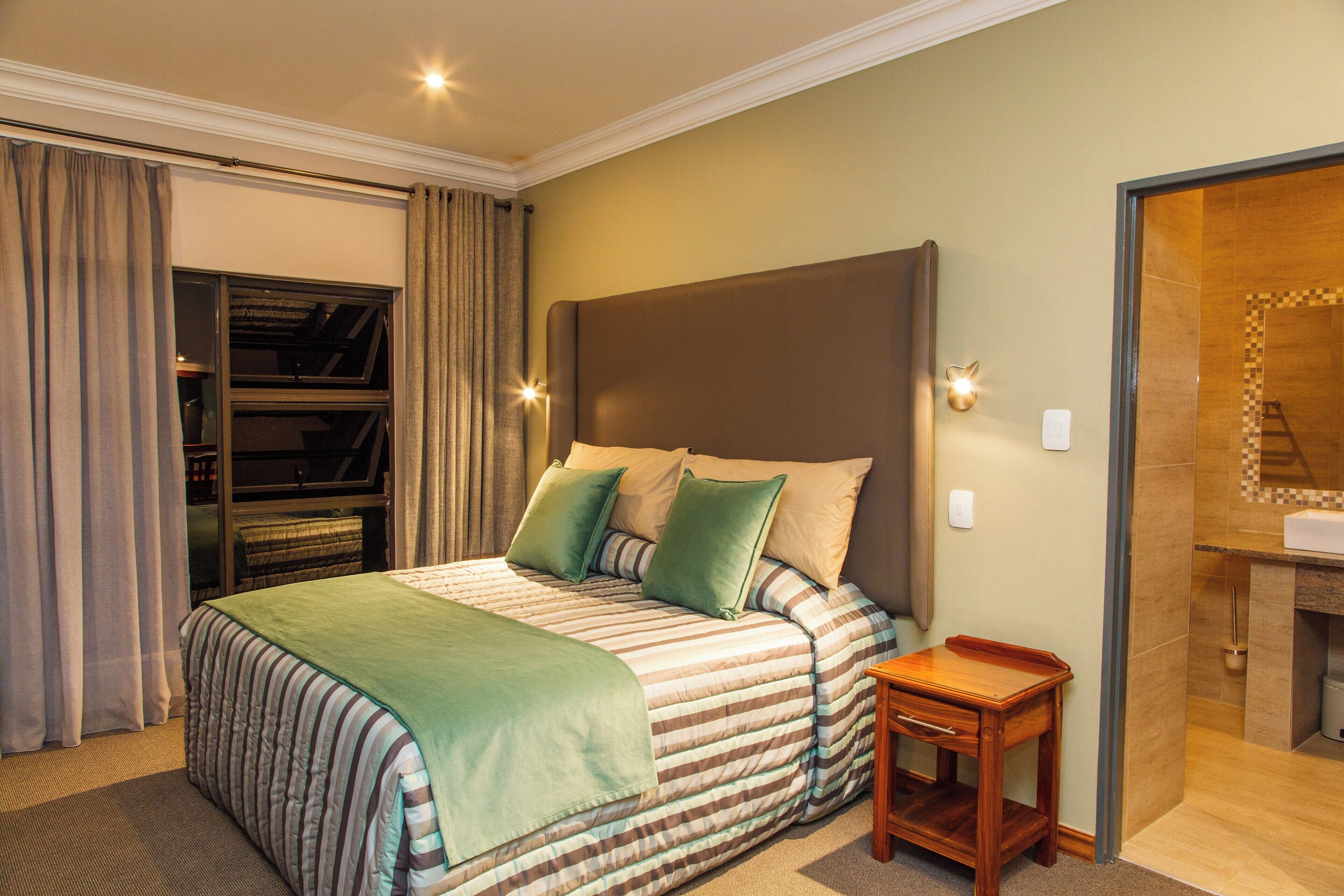 A hotel room with a large bed, a wooden nightstand, a closet with sliding doors, and a bathroom visible through an open door.