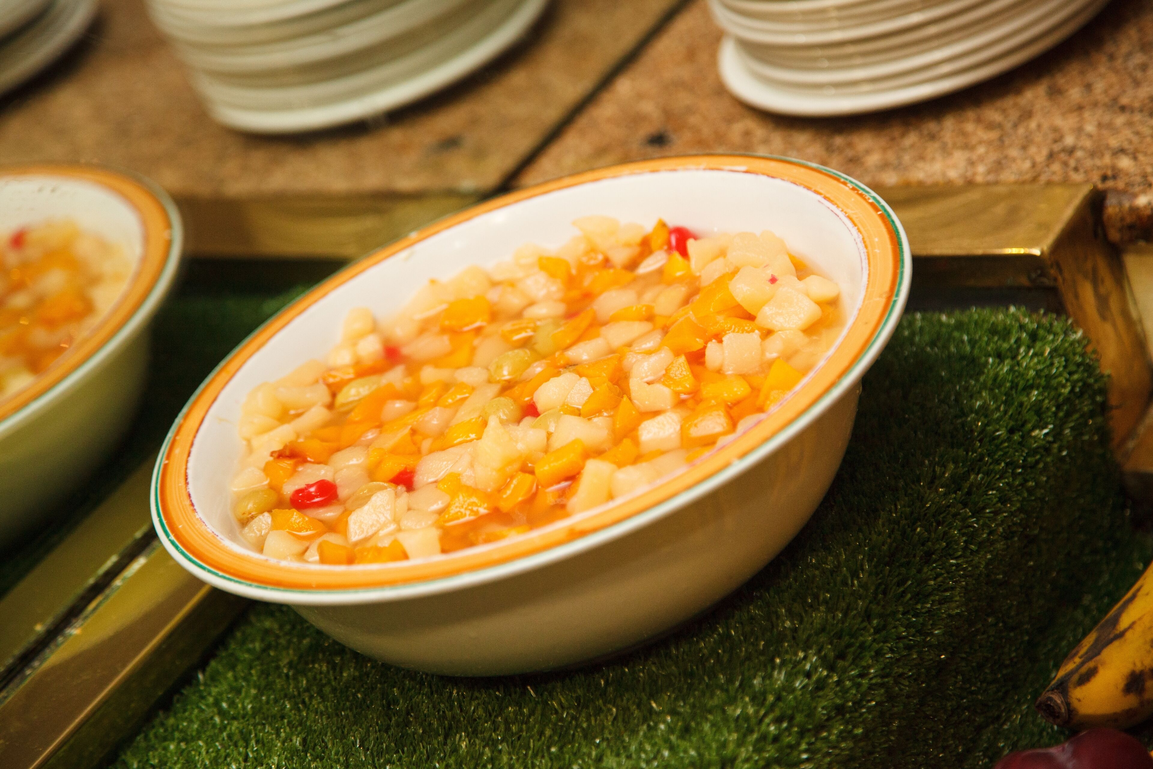 A bowl of diced fruit on a green surface with a wooden table in the background.
