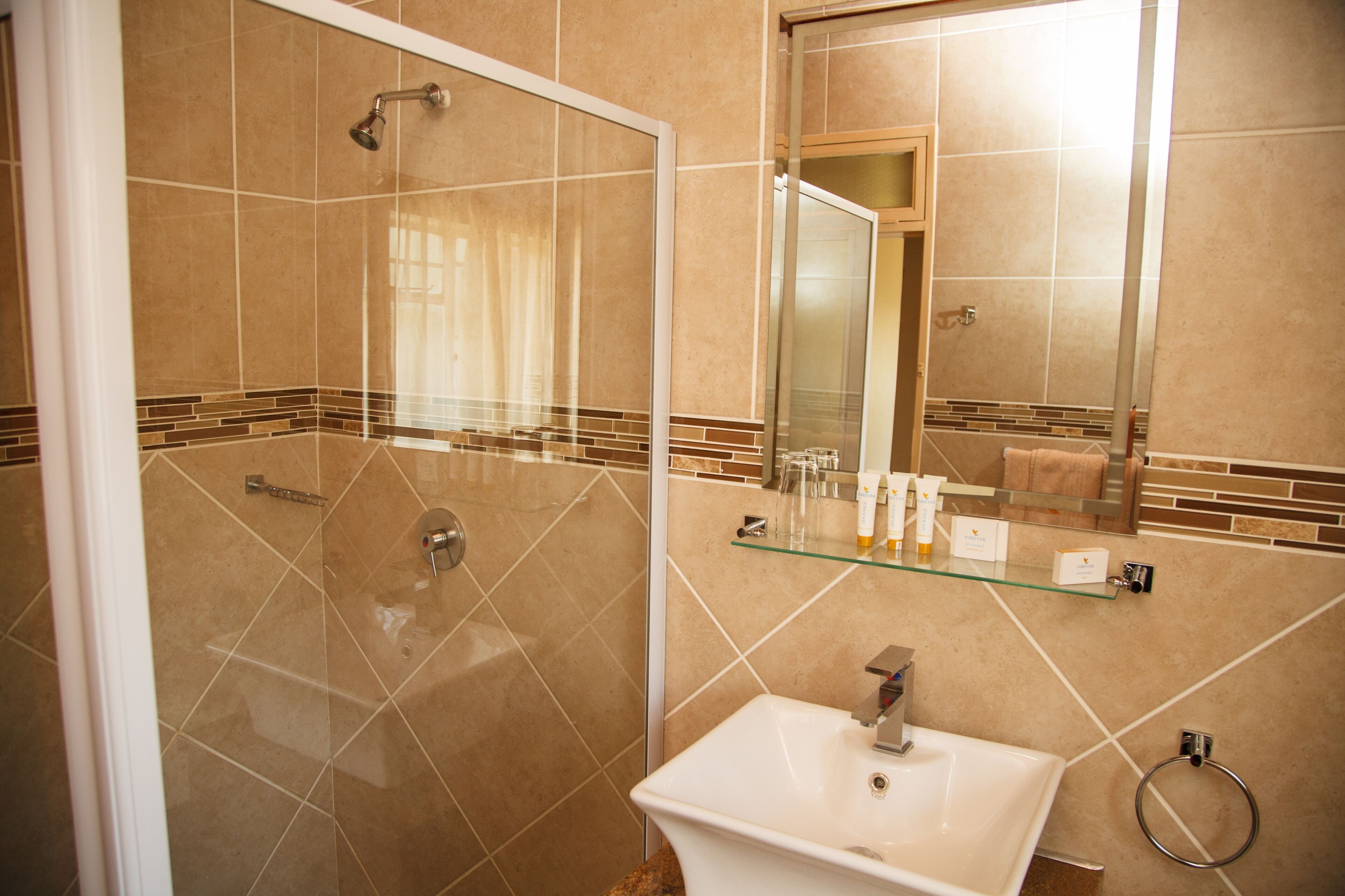 Un baño con cabina de ducha de vidrio, un lavamanos blanco y un estante de vidrio con artículos de aseo.