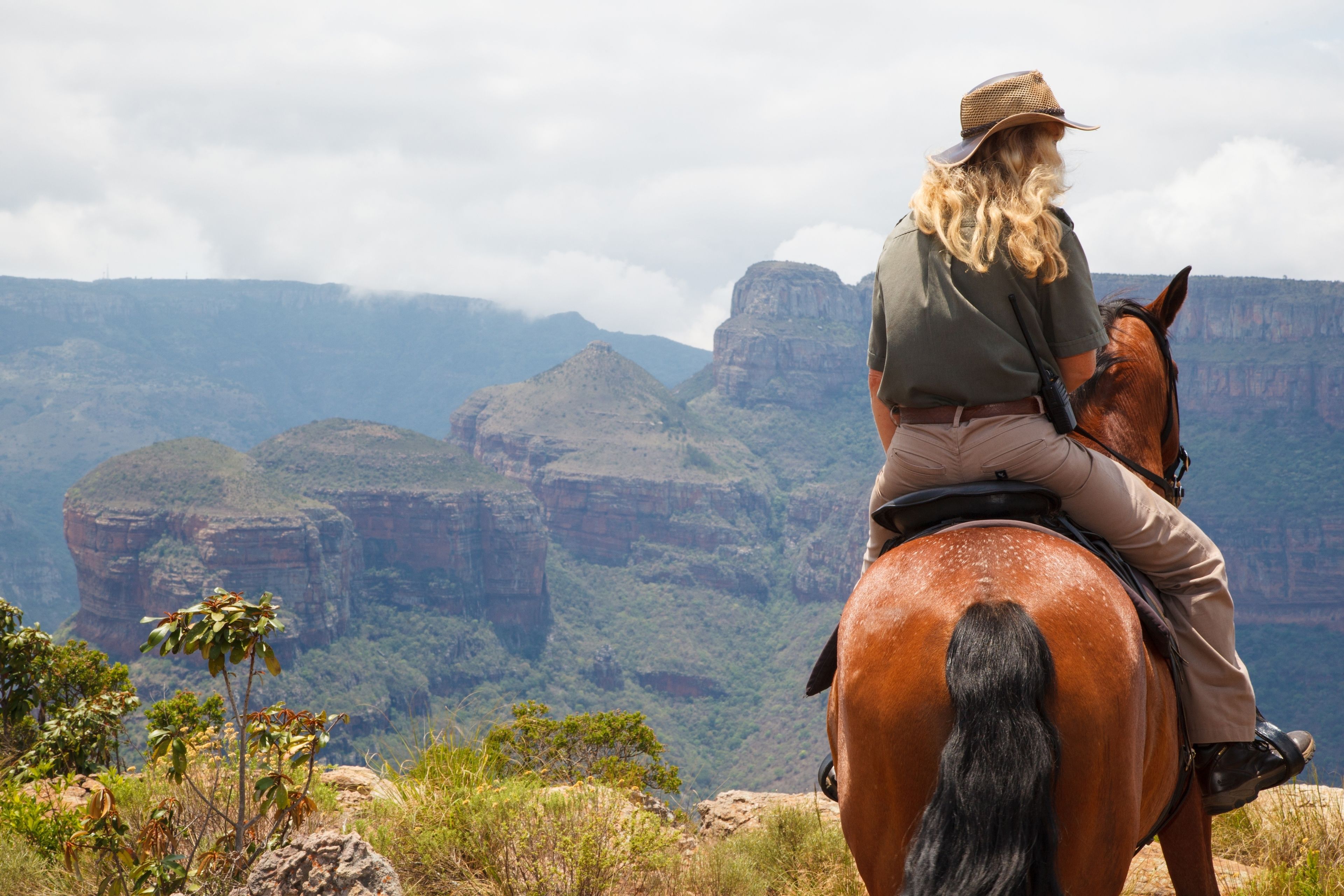 A person riding a horse on a mountain with a view of a canyon.